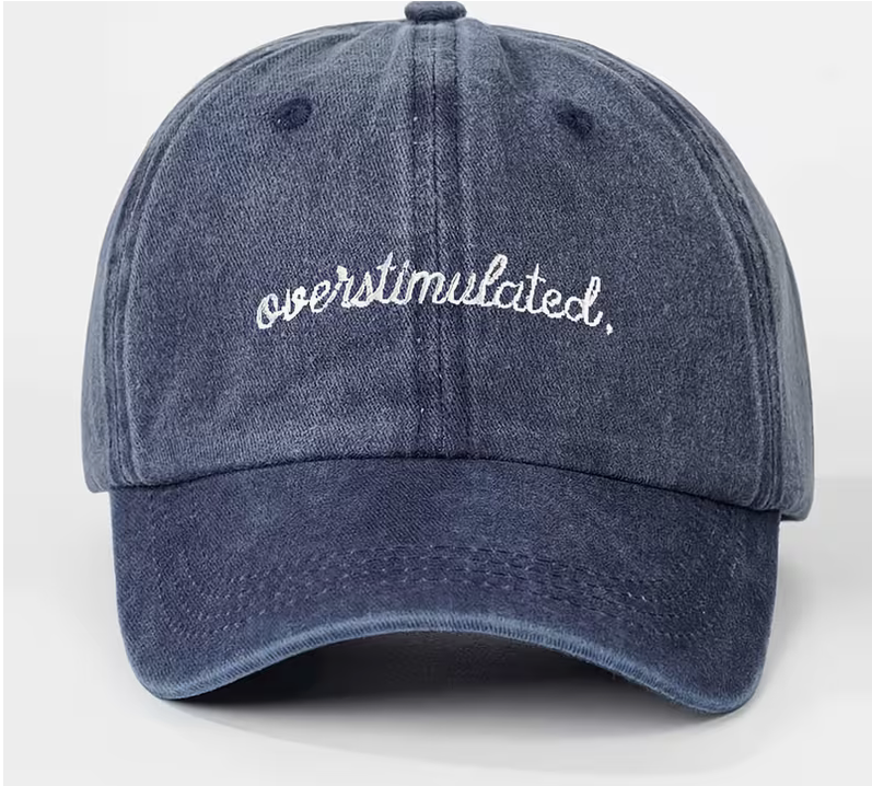 A washed blue denim baseball cap with 'overstimulated.' embroidered in white script across the front, shown against a light gray background.