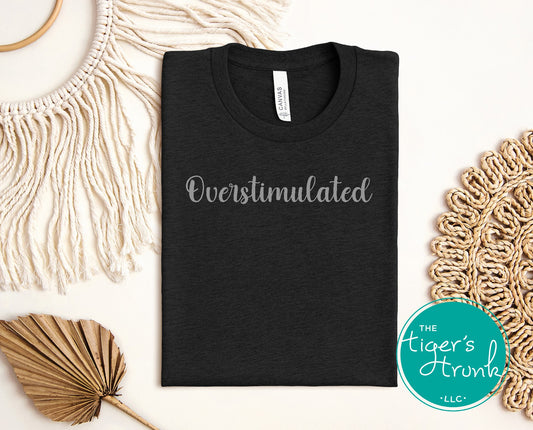 Black t-shirt with 'Overstimulated' text on a white background with decorative elements.