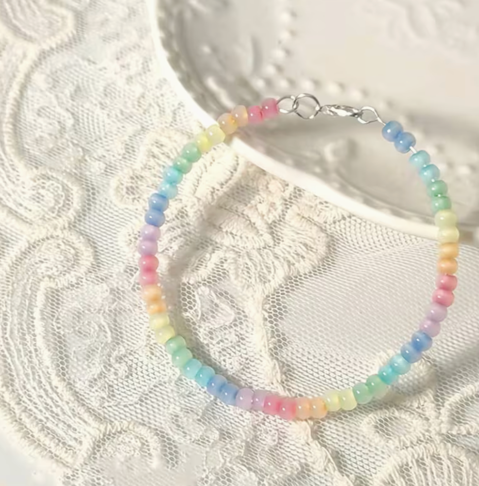 Pastel rainbow beaded bracelet with pink yellow green blue and lavender beads displayed on white lace