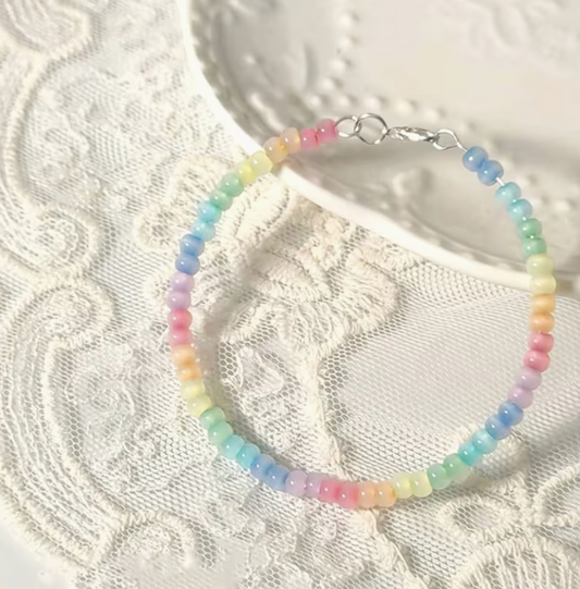 Pastel rainbow beaded bracelet with pink yellow green blue and lavender beads displayed on white lace