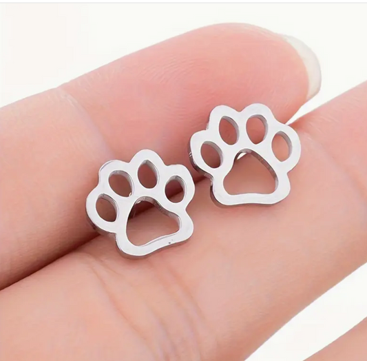 Silver paw print earrings held between fingers on a light skin background