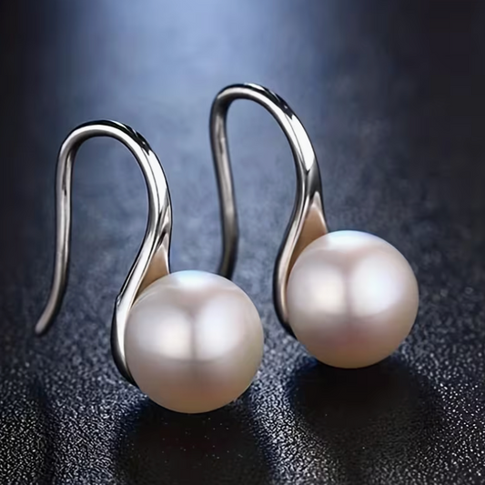 Silver tone pearl drop earrings with curved hook design on dark background
