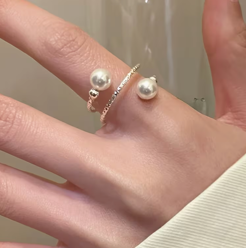 Silver tone adjustable wrap ring with symmetric faux pearl beads worn on a finger, showing the open fit and scale on hand.