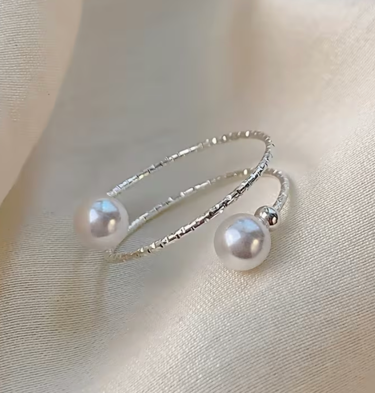 Silver tone adjustable wrap ring with two symmetric faux pearl round beads displayed on a soft neutral fabric background.