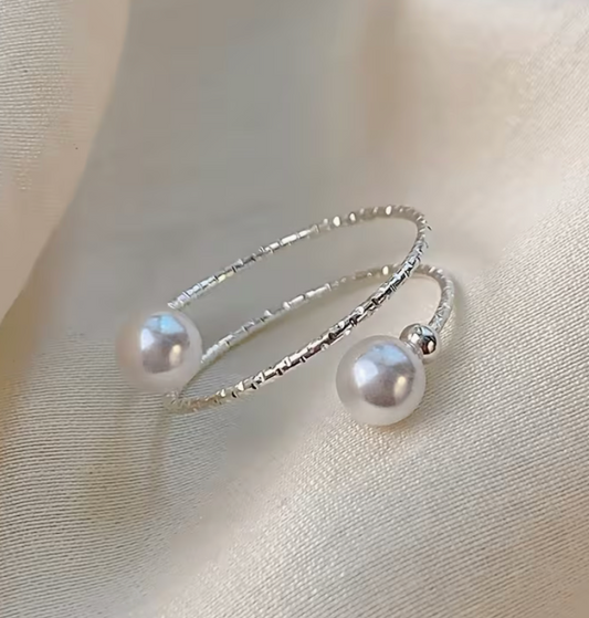 Silver tone adjustable wrap ring with two symmetric faux pearl round beads displayed on a soft neutral fabric background.