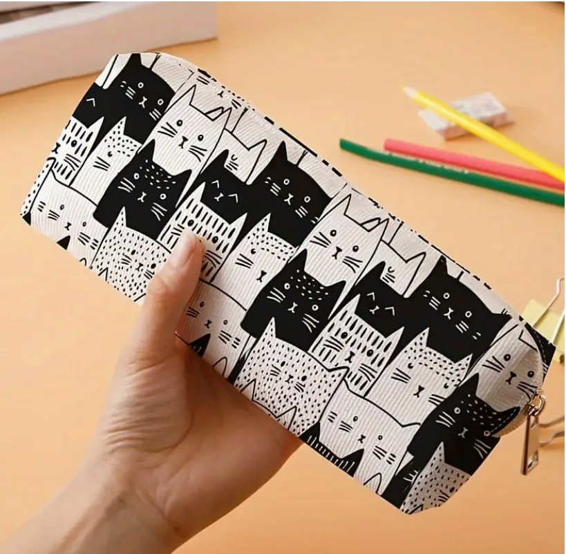 Pencil case with black cat pattern held by a hand on a wooden surface.
