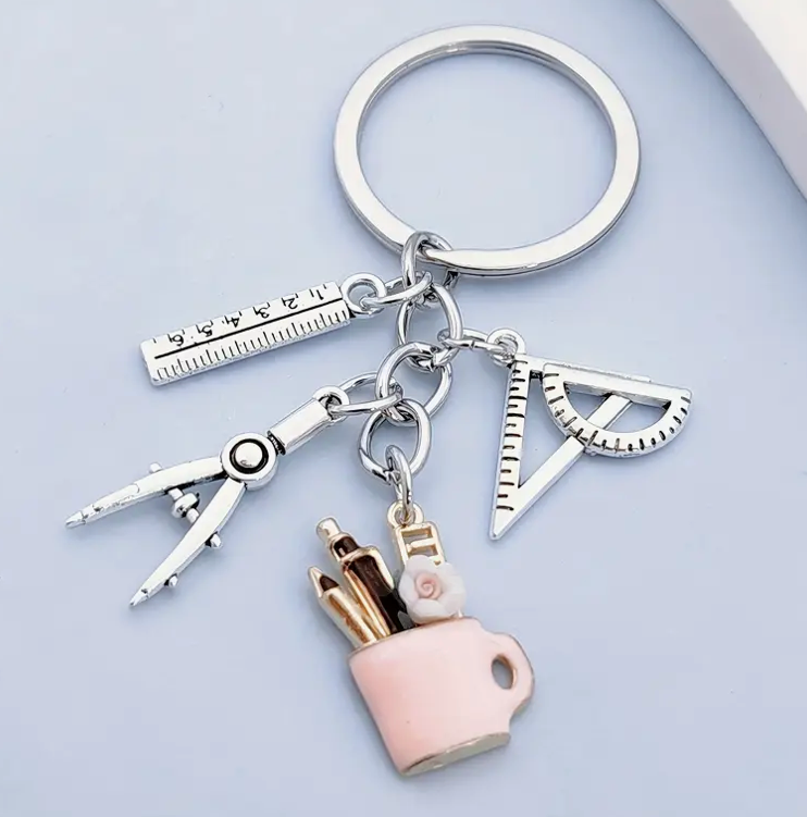 Metal keychain shaped like a mug filled with pens, a protractor, a compass, and a ruler—perfect for teachers and school staff.