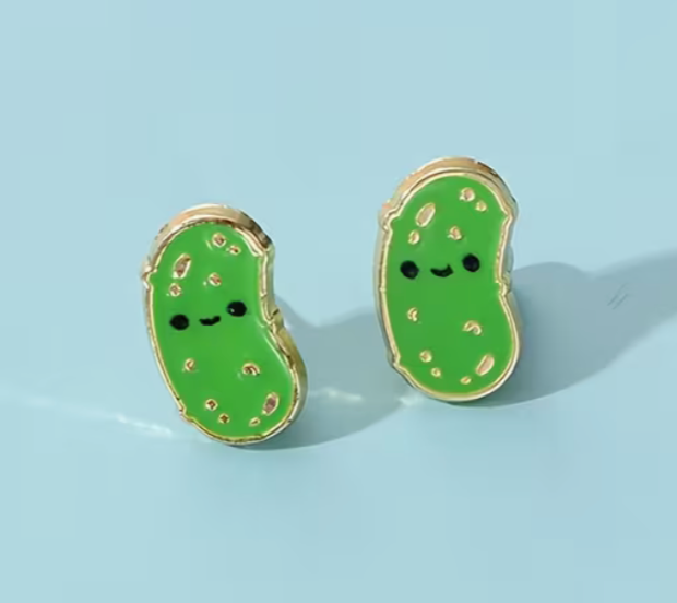 Green pickle-shaped earrings with smiling faces on a light blue background