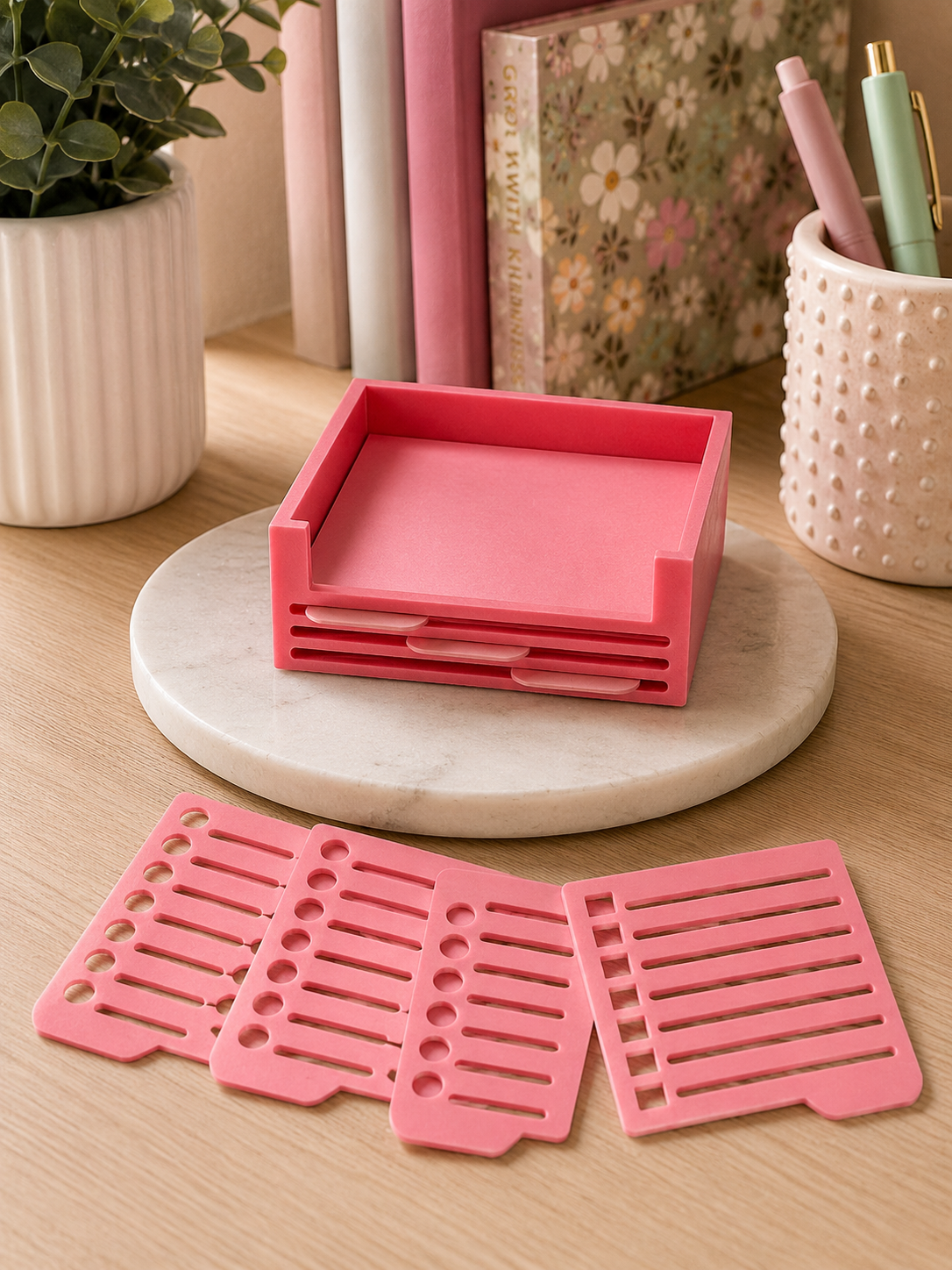 Pink 3D printed sticky note holder with interchangeable stencil inserts arranged beside the organizer on a desktop.