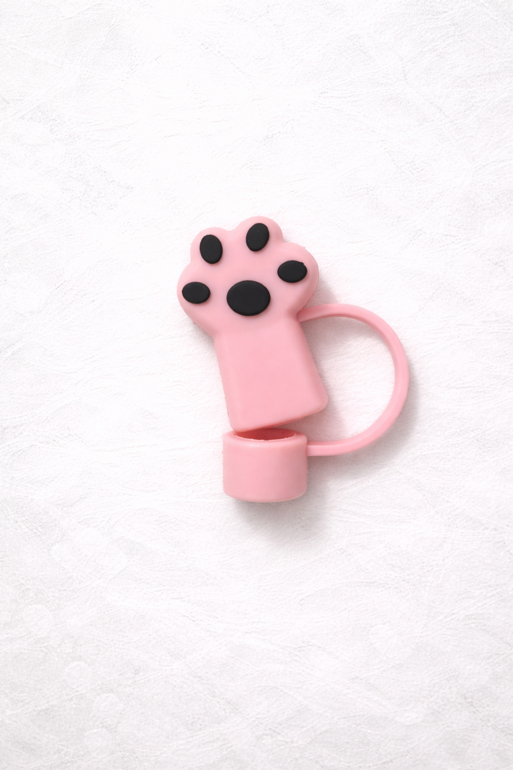 Pink silicone straw topper shaped like a cat paw with black paw pad details and flexible loop attachment for reusable tumbler straw.