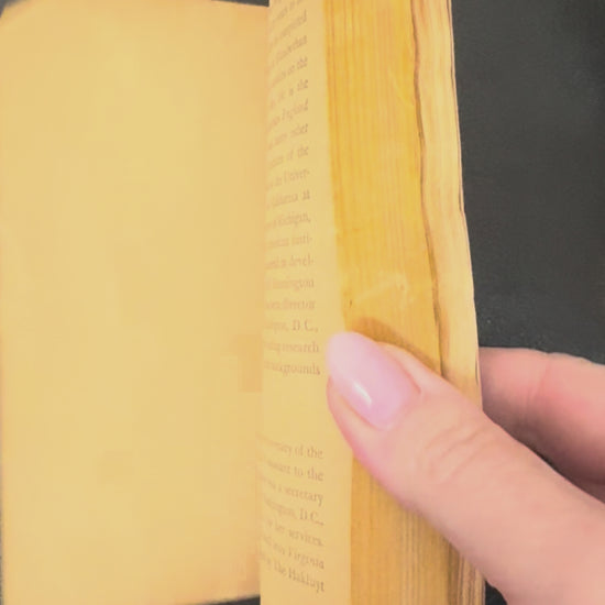 Book titled 'The Merchant of Venice' by William Shakespeare on a wooden stand with a plant in the background.