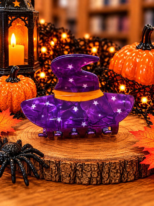Purple witch hat Halloween hair claw clip measuring approximately 3 inches, featuring white stars, an orange hatband, and purple claw teeth, displayed with pumpkins and festive Halloween decorations.