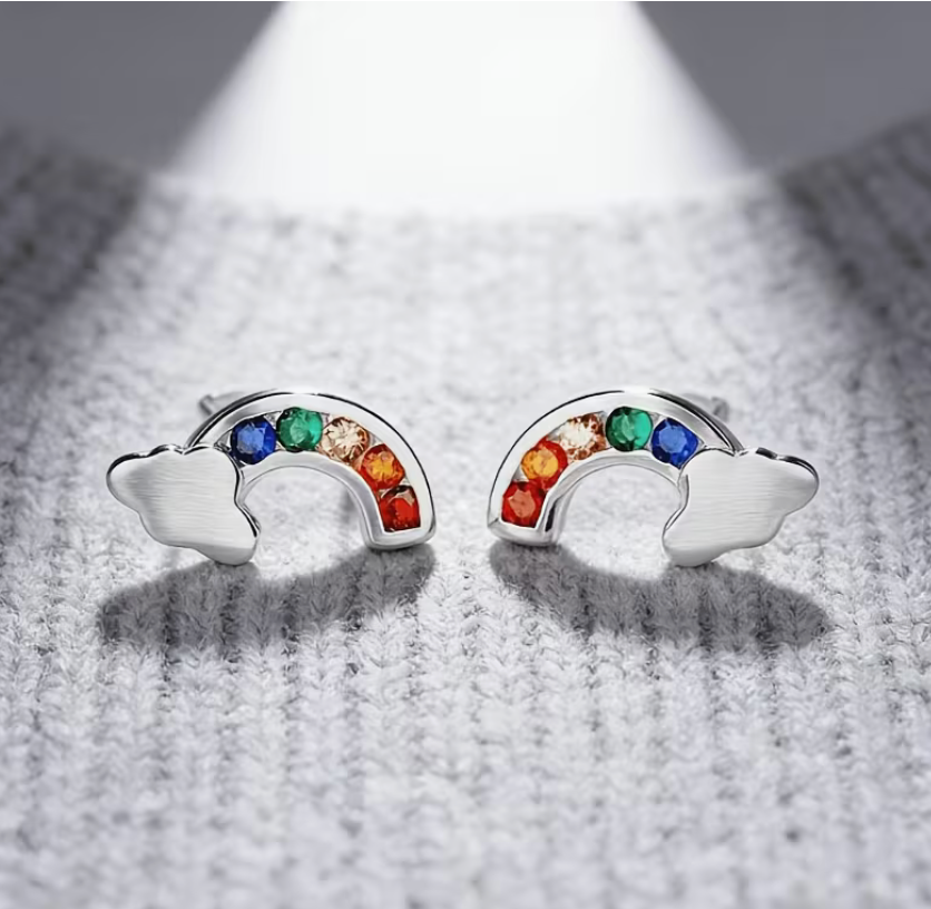 Pair of silver-tone rainbow cloud stud earrings featuring colorful cubic zirconia stones in a rainbow arc design on a textured gray background.