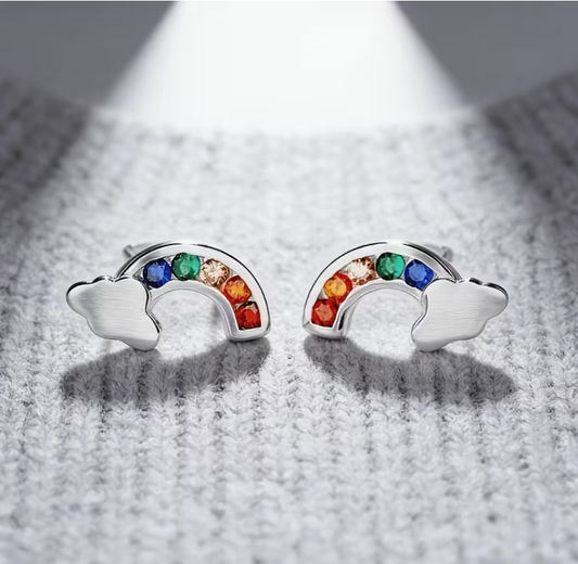 Pair of silver-tone rainbow cloud stud earrings featuring colorful cubic zirconia stones in a rainbow arc design on a textured gray background.