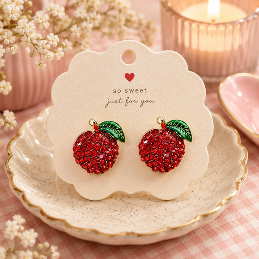 Pair of sparkling raspberry stud earrings with red crystal berries and green leaf accents displayed on a decorative jewelry card.