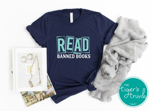 Navy blue t-shirt with 'READ BANNED BOOKS' text, book, and gray pants on a white background.