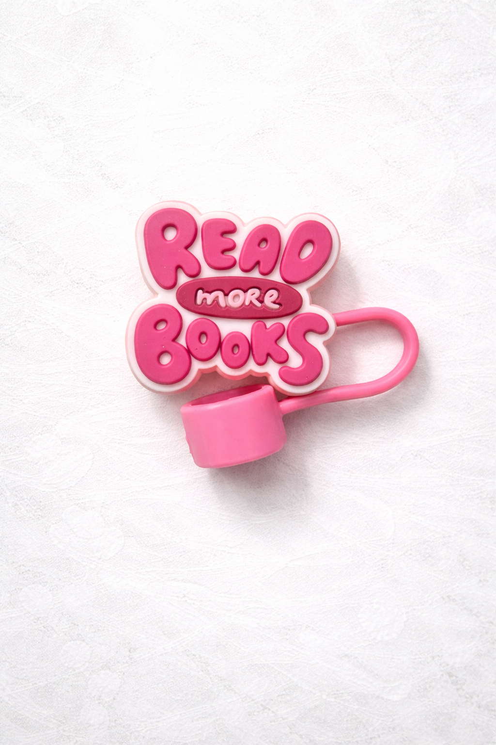 Pink silicone straw topper with raised lettering that says Read More Books, attached to a flexible loop for reusable tumbler straw.