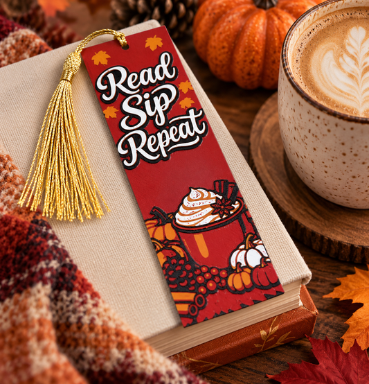 Read Sip Repeat fall bookmark with red autumn background, coffee and pumpkin illustrations, and gold tassel displayed on a book beside a cozy latte.