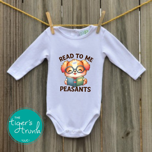 White long-sleeve baby bodysuit hanging on a clothesline with a cute puppy holding a book and the phrase Read to Me Peasants.