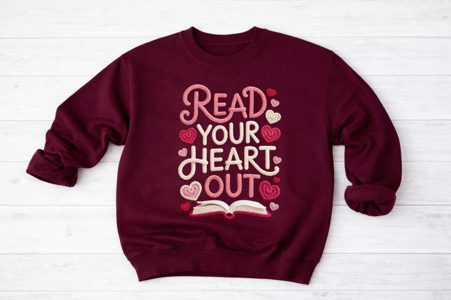 Maroon sweatshirt with 'Read Your Heart Out' text and heart designs on a white wooden surface