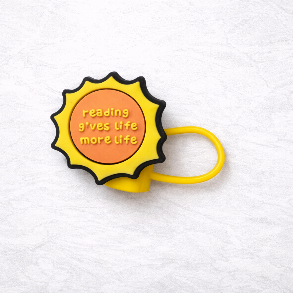 Yellow sun-shaped silicone straw topper with the phrase “reading gives life more life,” attached to a matching yellow flexible loop for reusable tumbler straw.