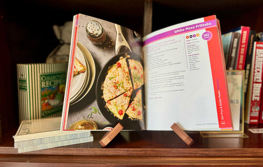 Open cookbook on a wooden surface with other books in the background