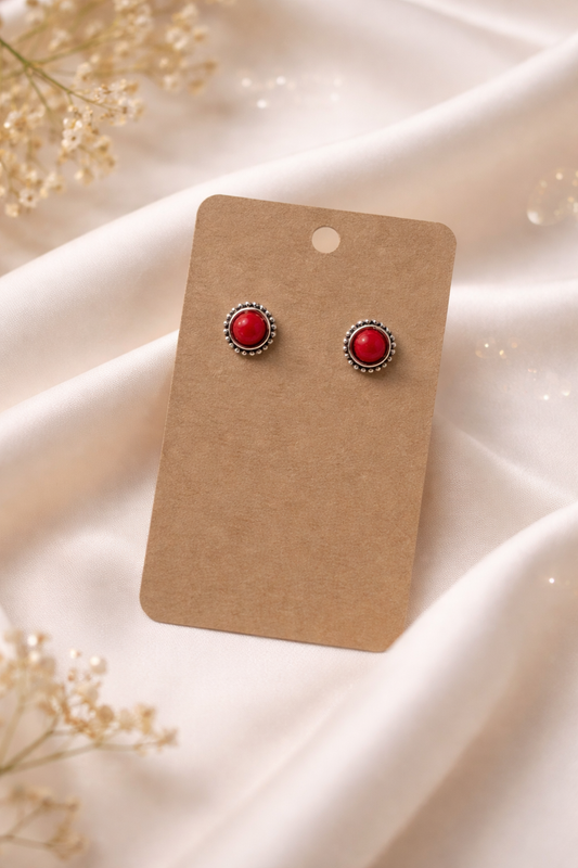 Red stud earrings with silver tone setting displayed on a neutral card with a soft light background