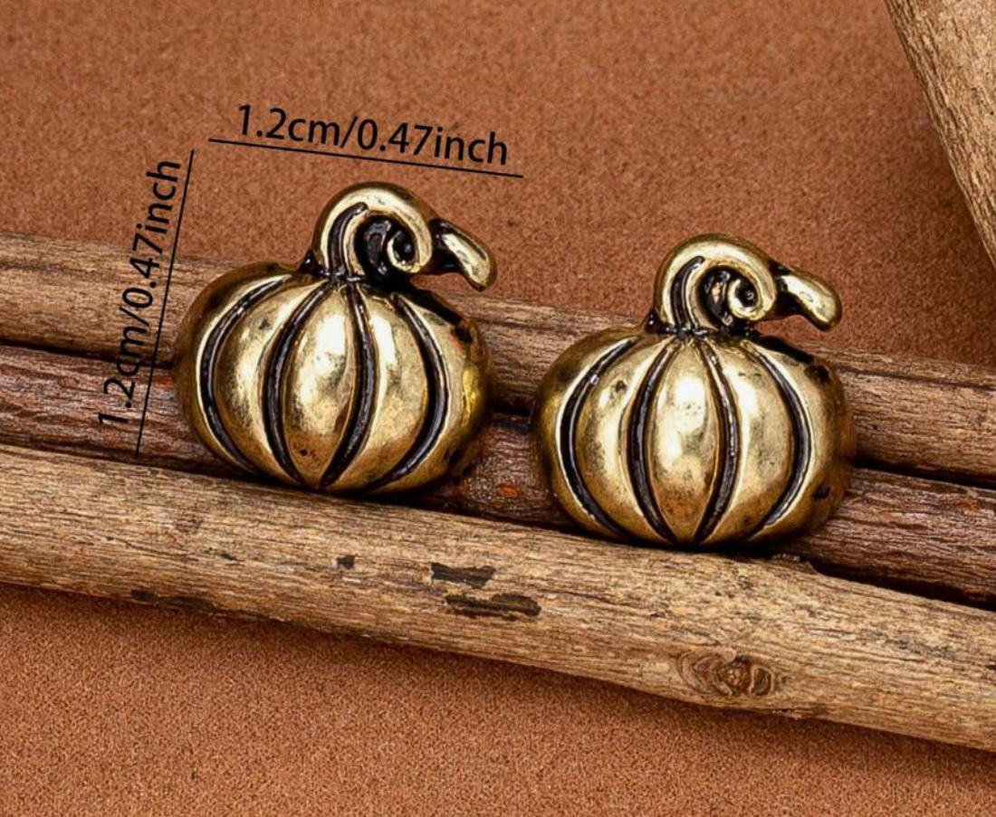 Two gold pumpkin-shaped earrings on a wooden stick with measurements.