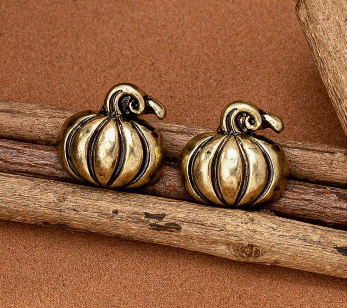 Pair of gold pumpkin-shaped earrings on wooden sticks with a brown background