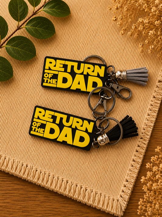 Set of Return of the Dad 3D printed dad keychains with black and gray tassels on textured beige background