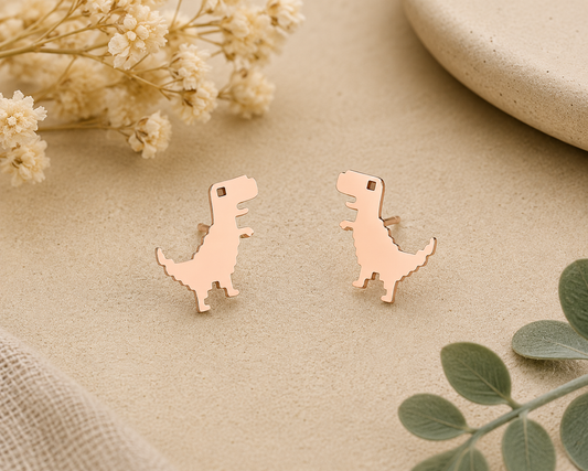 Tiny rose gold dinosaur stud earrings with minimalist T-Rex silhouette displayed on a neutral background with soft floral accents