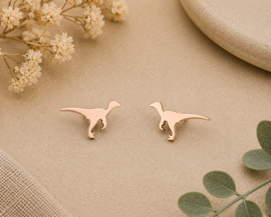 Tiny rose gold raptor stud earrings with minimalist dinosaur silhouette displayed on a neutral background with floral accents