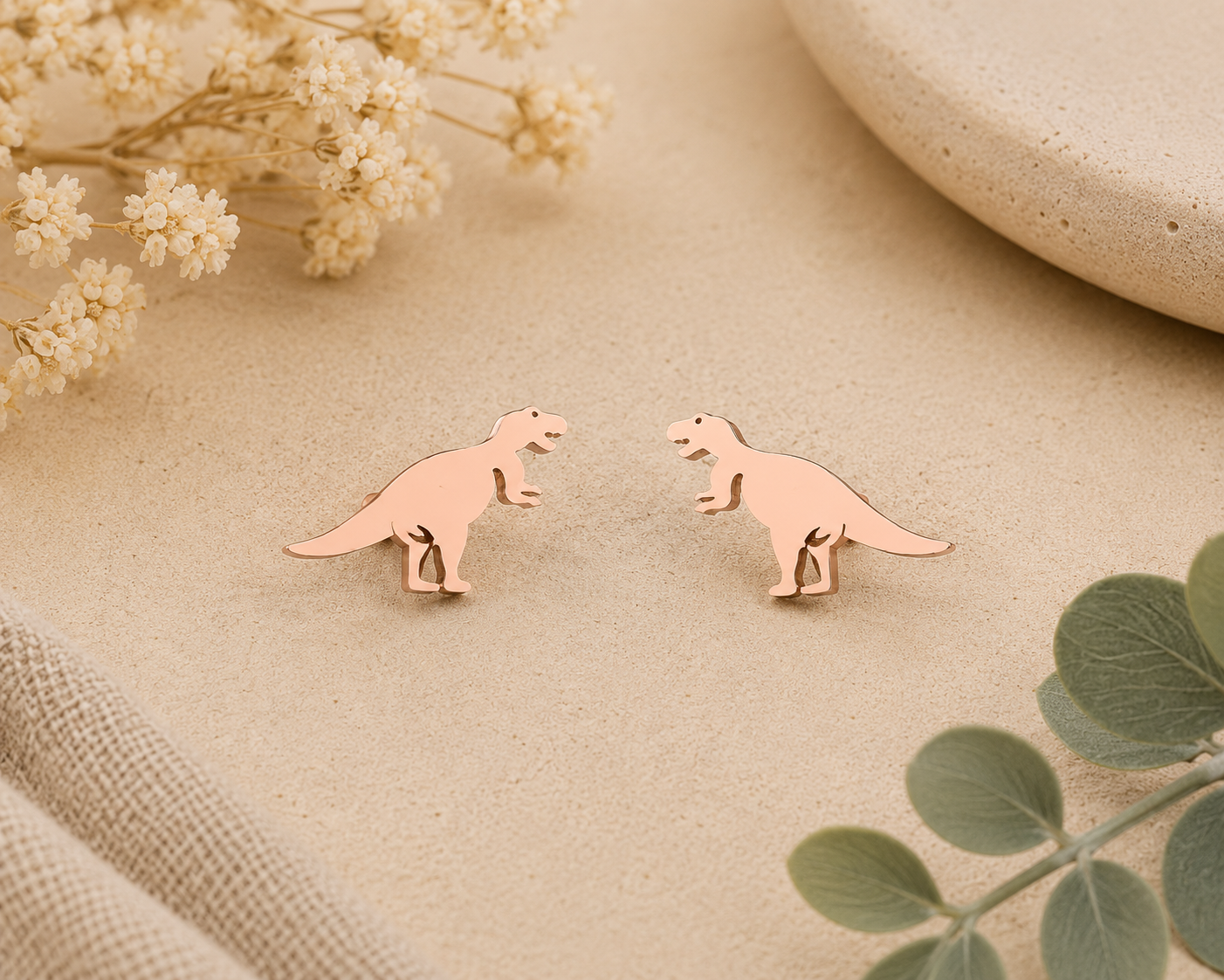 Tiny rose gold T-Rex stud earrings with minimalist dinosaur silhouette displayed on a neutral background with floral accents