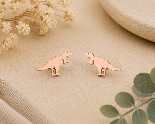 Tiny rose gold T-Rex stud earrings with minimalist dinosaur silhouette displayed on a neutral background with floral accents