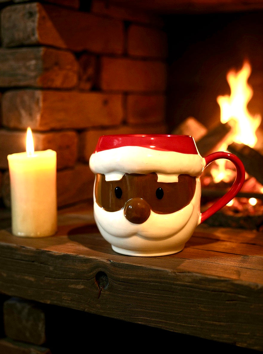 Santa Claus mug on a wooden surface with a lit candle and fireplace in the background