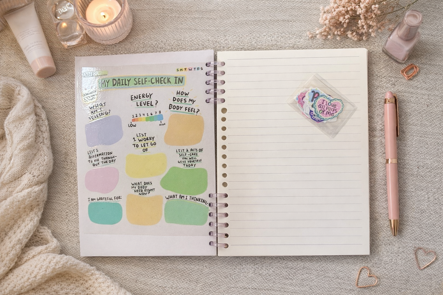 Open self love journal showing a laminated daily self check in page beside a lined notebook page, styled in a cozy flat lay with a pink pen, candle, nail polish, and affirmation stickers.