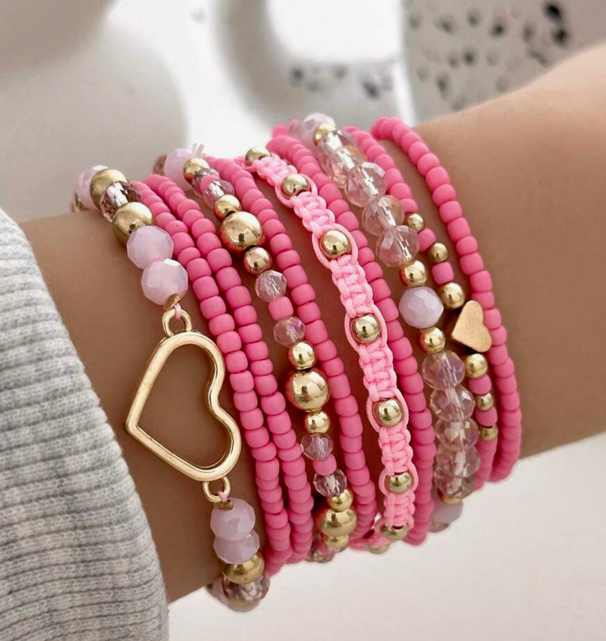 Multiple pink beaded bracelets with gold accents on a wrist.