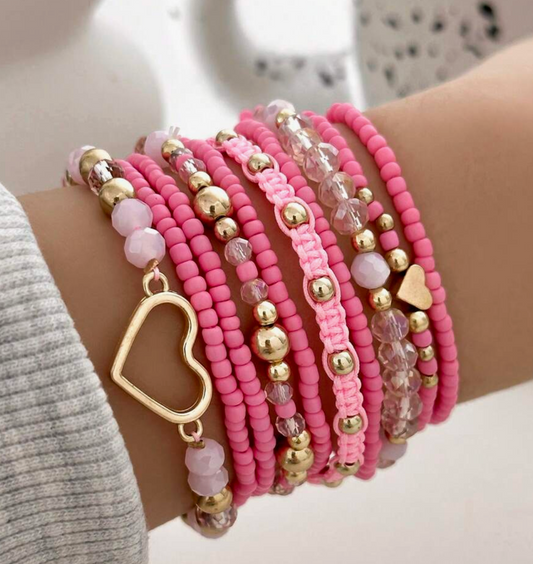 Multiple pink beaded bracelets with gold accents on a wrist.