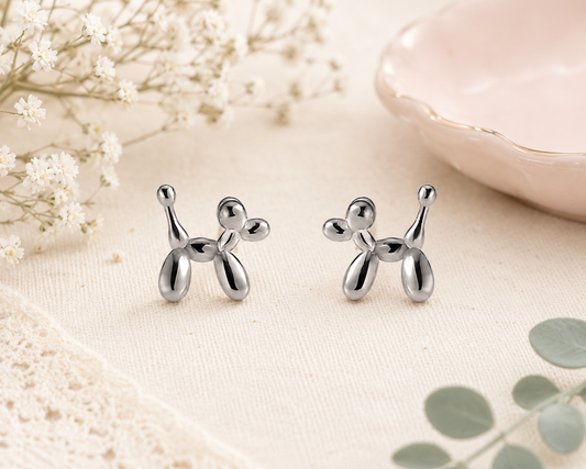 Silver balloon dog stud earrings with polished balloon animal design displayed on a neutral background with soft floral accents