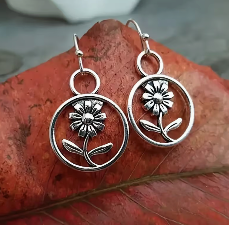Silver-tone daisy drop earrings with open circle frames, flower stems and leaves in a vintage boho style.