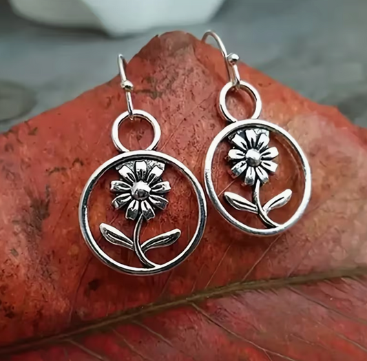 Silver-tone daisy drop earrings with open circle frames, flower stems and leaves in a vintage boho style.