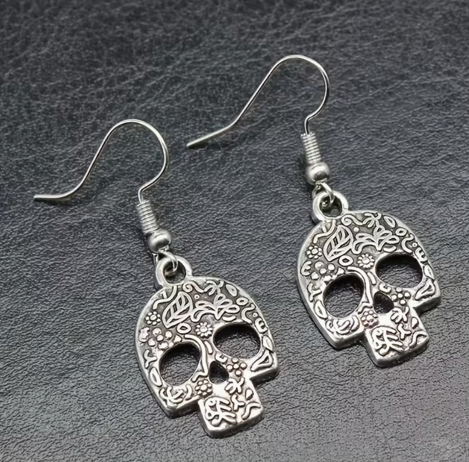 Silver-tone skull earrings with detailed floral and leaf pattern on a dark background