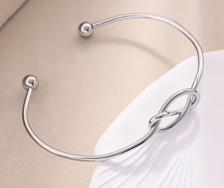 Silver-tone adjustable open cuff bracelet featuring an elegant knot design and polished ball ends.