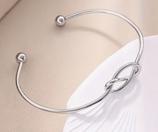 Silver-tone adjustable open cuff bracelet featuring an elegant knot design and polished ball ends.