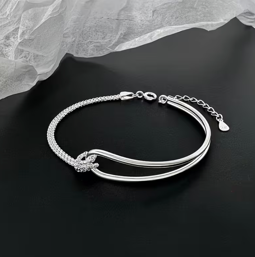 Minimalist silver knot bracelet with layered chain detail displayed on a black background.