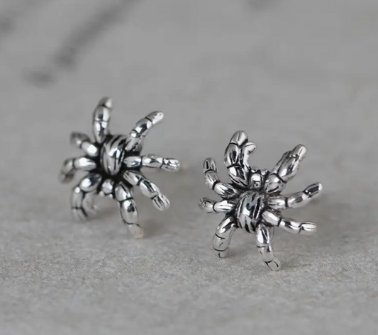 Silver spider-shaped earrings on a gray background