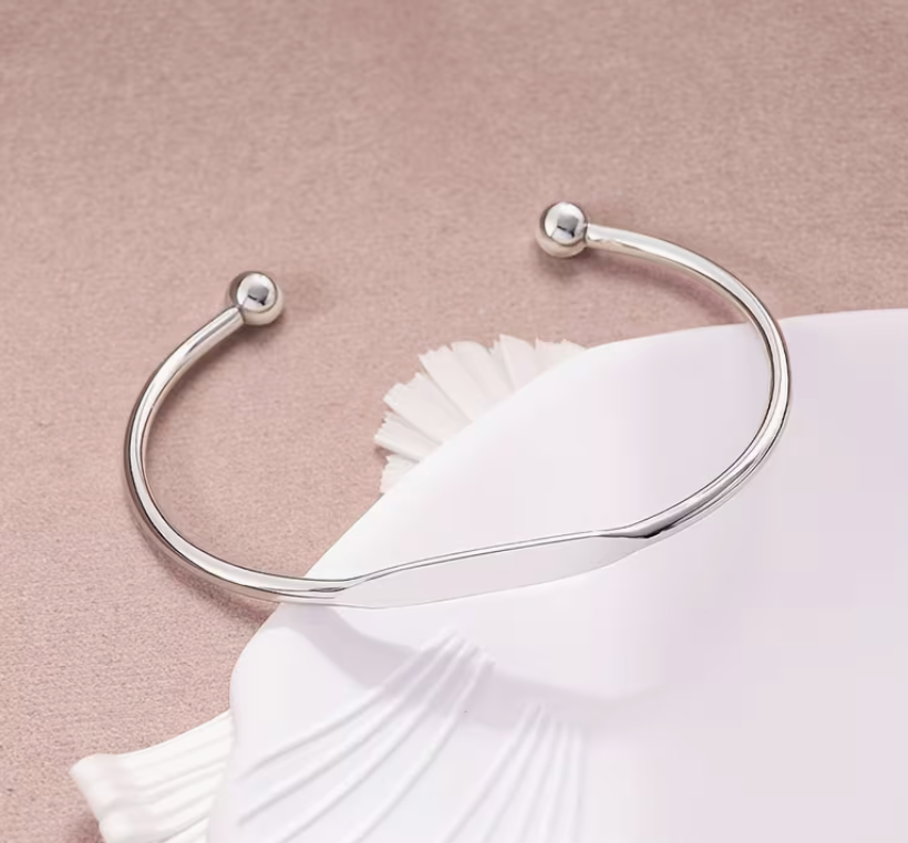 Silver-tone adjustable cuff bracelet featuring a graceful twisted center design and polished ball ends.