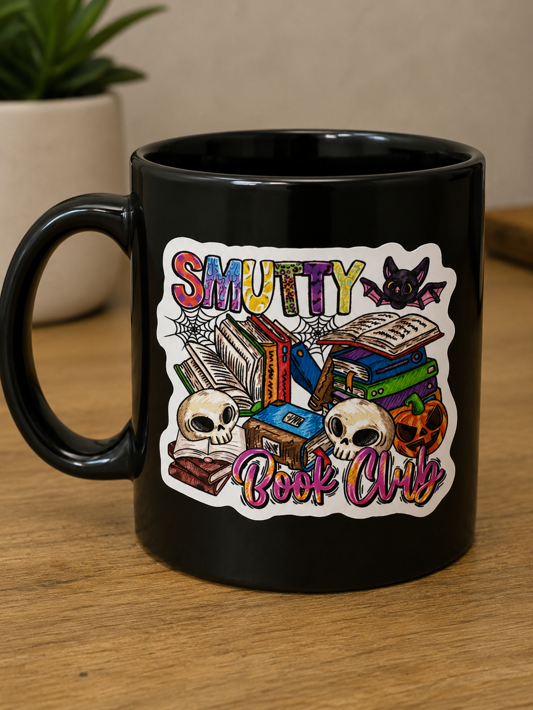 Colorful Smutty Book Club die cut sticker featuring stacked books, skulls, a bat, and a pumpkin displayed on a black mug.