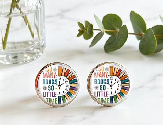 Pair of round silver-tone stud earrings featuring colorful books arranged around a clock and the saying So Many Books So Little Time beneath glossy domed fronts.