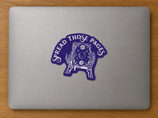 Purple die cut sticker featuring a mystical book with skeletal hands and the phrase "Spread Those Pages" displayed on a laptop.